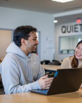 Two people smiling at each other in front of a laptop
